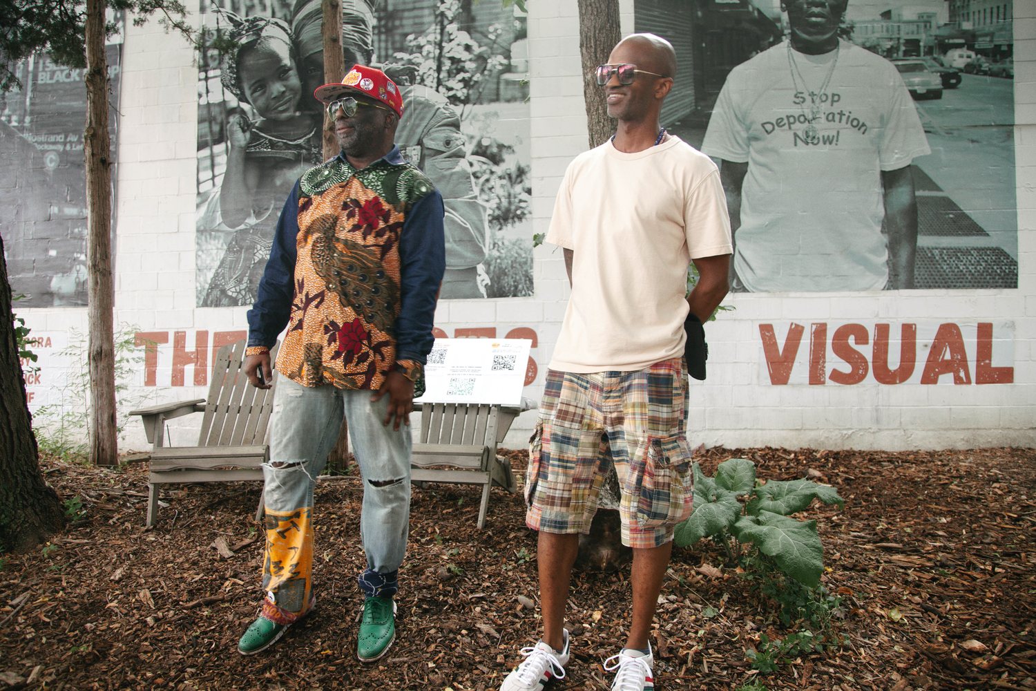 Russell Frederick and Dahkil Hausif standing in front of the mural at the Seeds of Somers Garden, both looking off camera and laughing.