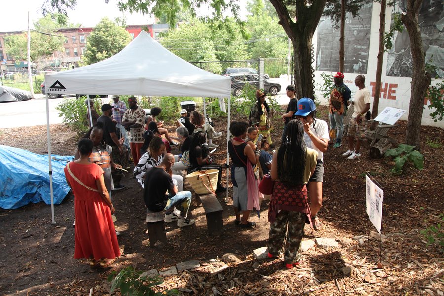 A crowd gathered under a white canopy in the garden beside the mural wall.