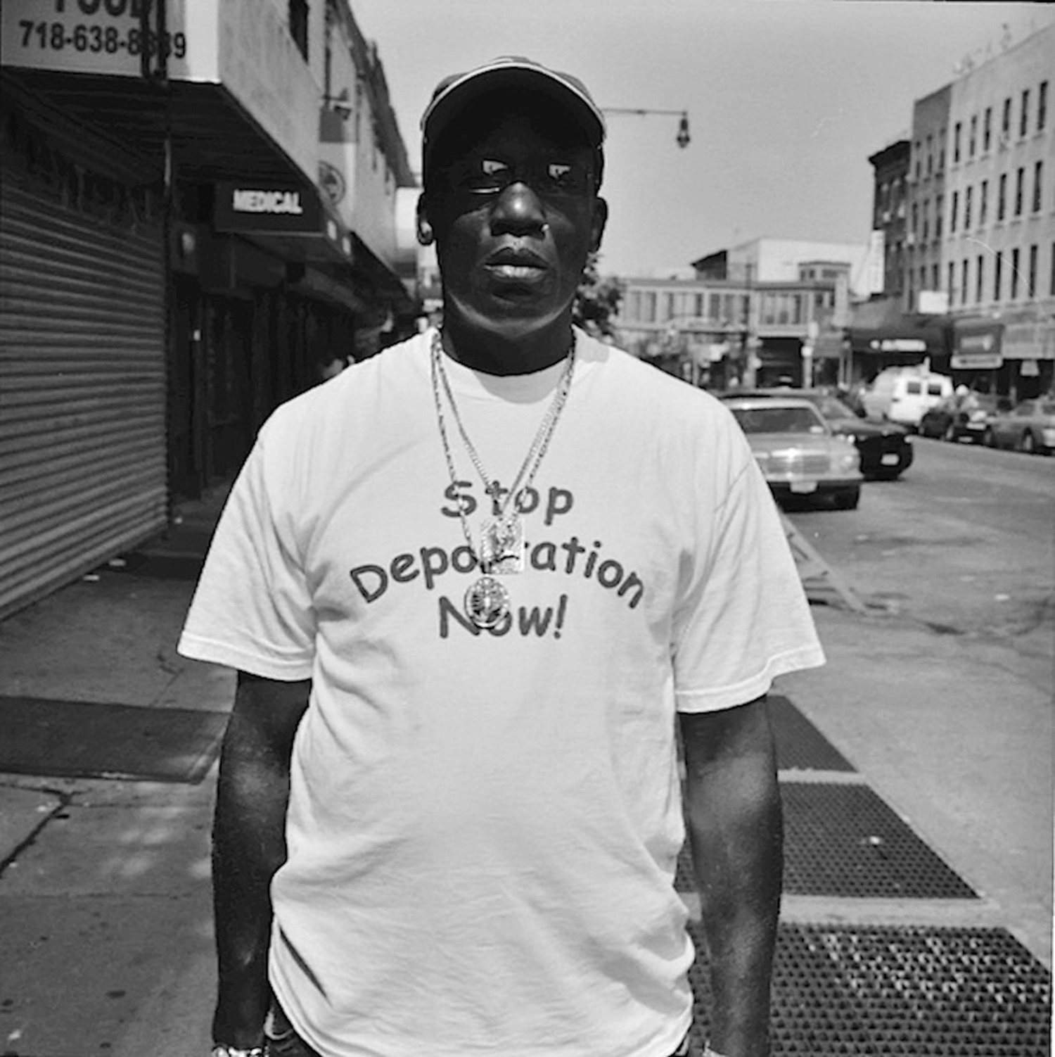 Stop Deportation, 2007. A man stands on a Brooklyn sidewalk wearing a T-shirt reading Stop Deportation Now.